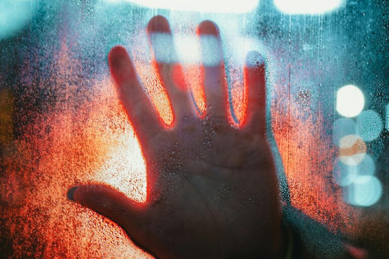 A dramatic depiction of a hand pressed against a foggy, illuminated window.